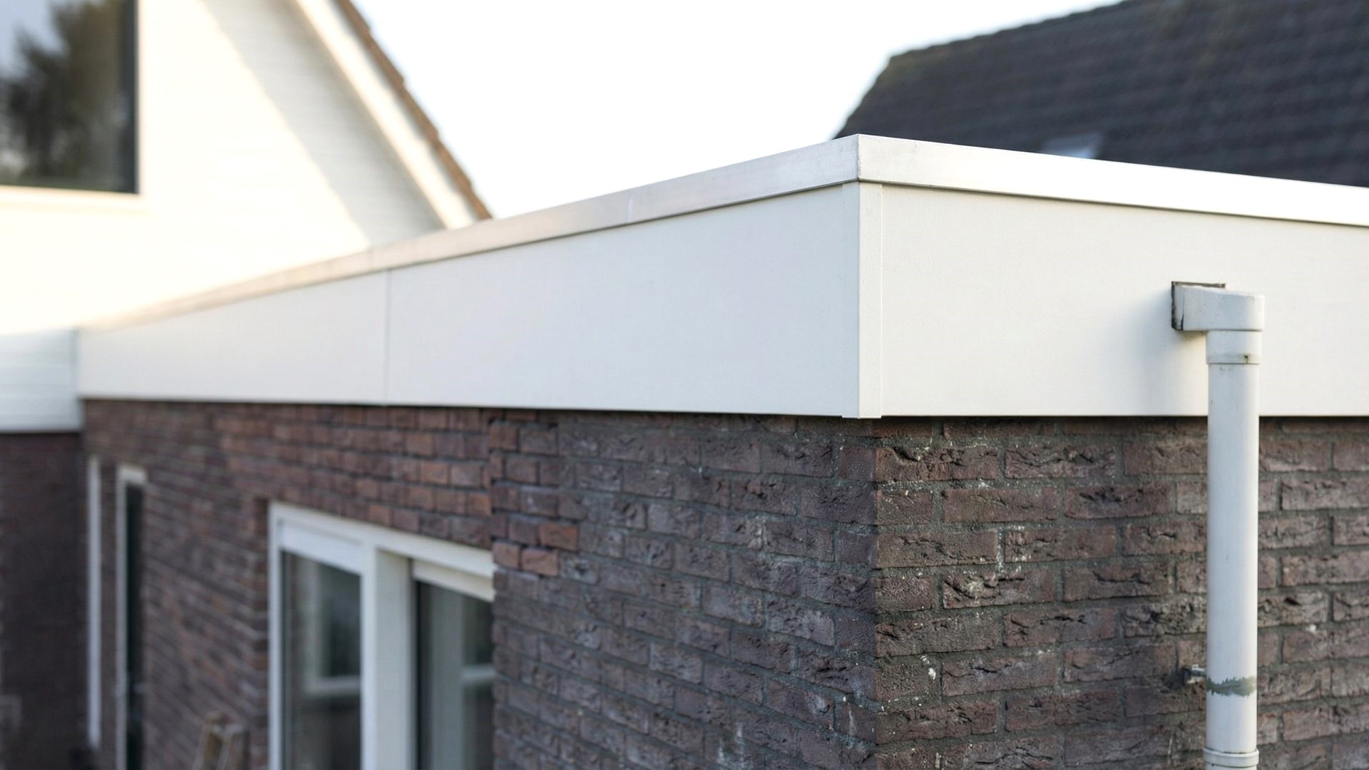 Keralit dakrandpaneel 350 in wit gemonteerd op aanbouw met bakstenen gevel en strakke afwerking 